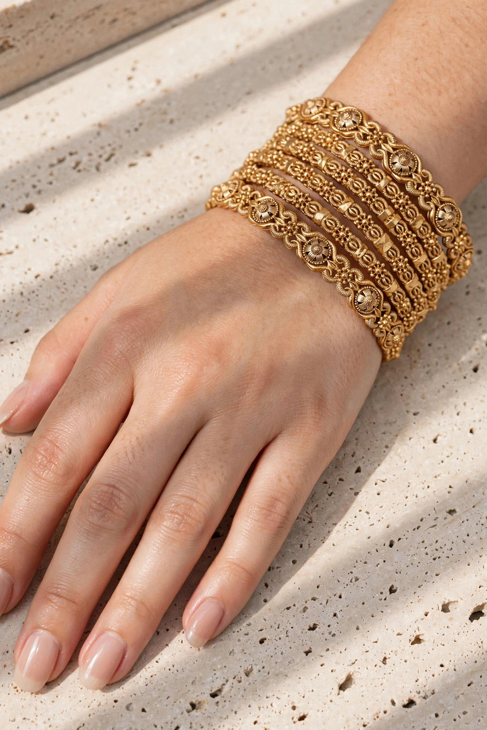 Woman hand wearing set of 6 antique gold kundan rajwadi bangles on travertine stone background - Jewel Galore Pakistan
