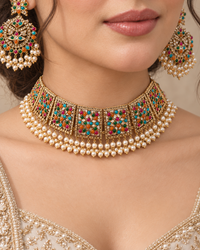 A close-up of a model wearing an ornate gold choker necklace with multicolored stones and double rows of pearls, along with matching earrings.